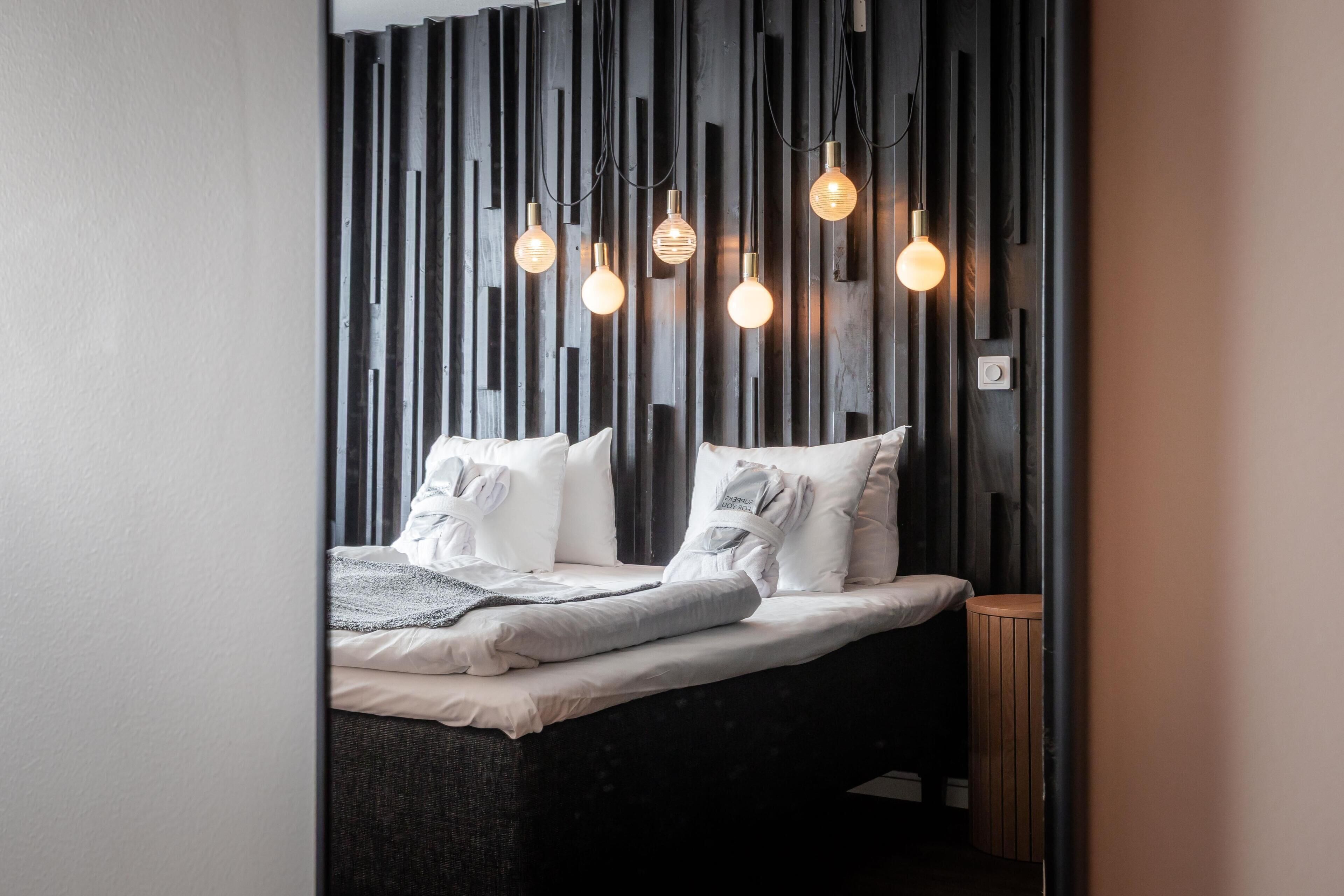 A modern bedroom with a bed, bedside tables, and a wall with vertical wooden slats.