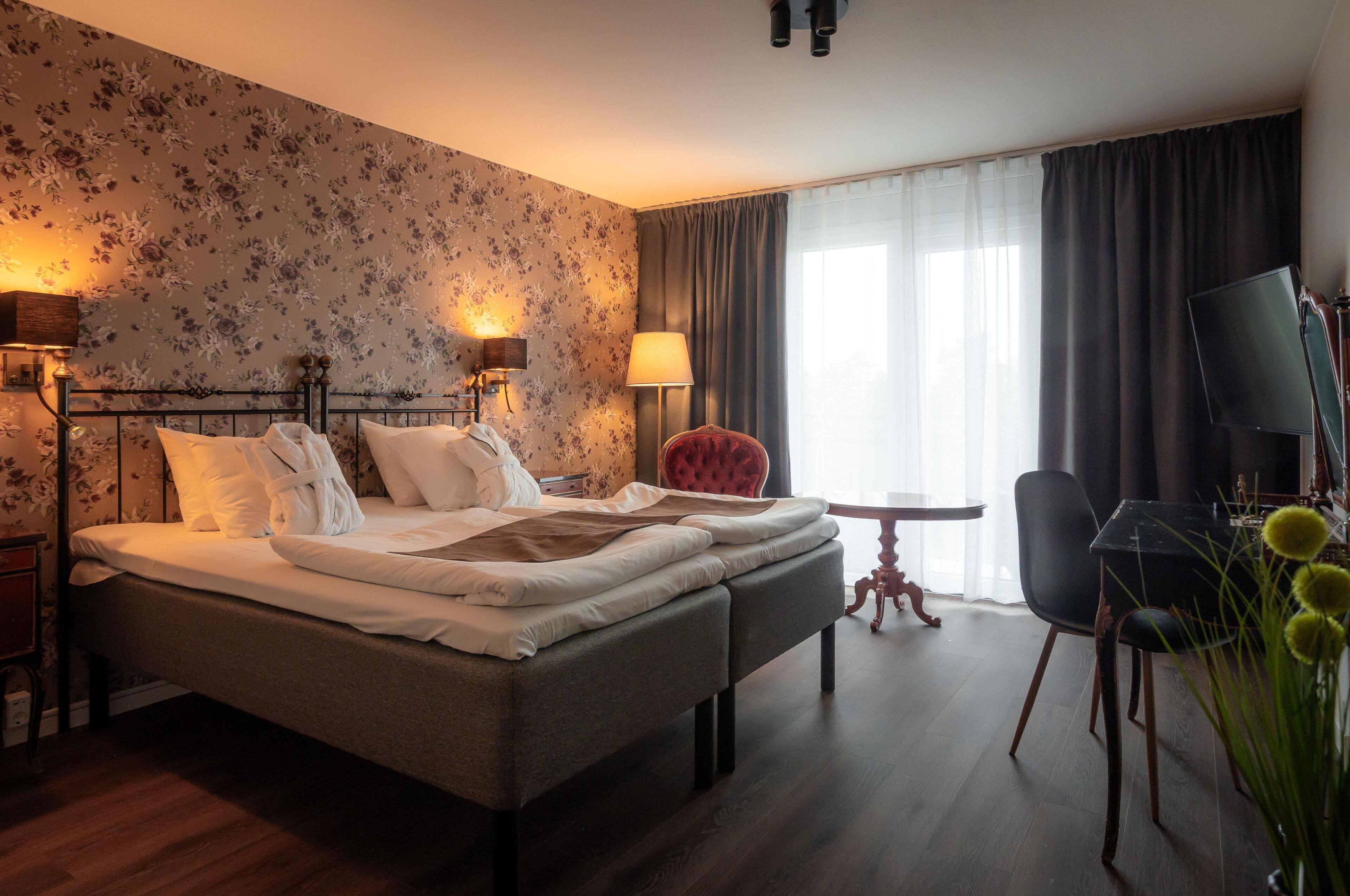 Ett hotellrum med en säng, ett skrivbord, en stol, en lampa och en tv.