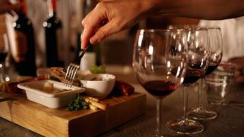 A dining table with a wooden board, a white bowl, and a fork. There are wine glasses and bottles in the background.