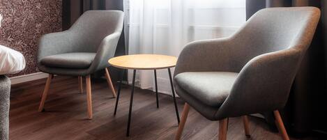 A room with two grey armchairs, a small round table, and a window with sheer curtains.