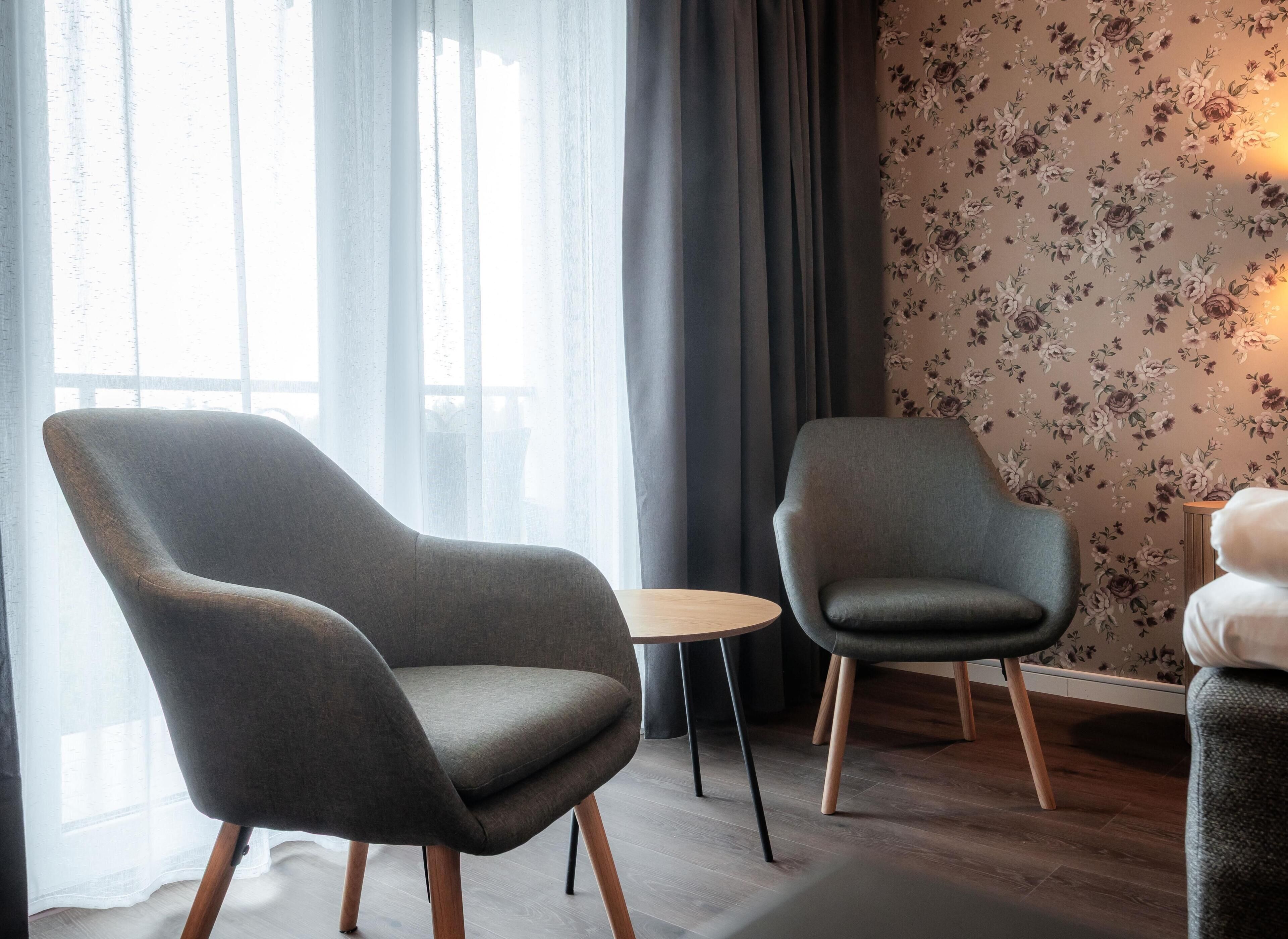 Una habitación moderna con dos sillones grises, una mesita redonda y un estampado floral en el papel tapiz.