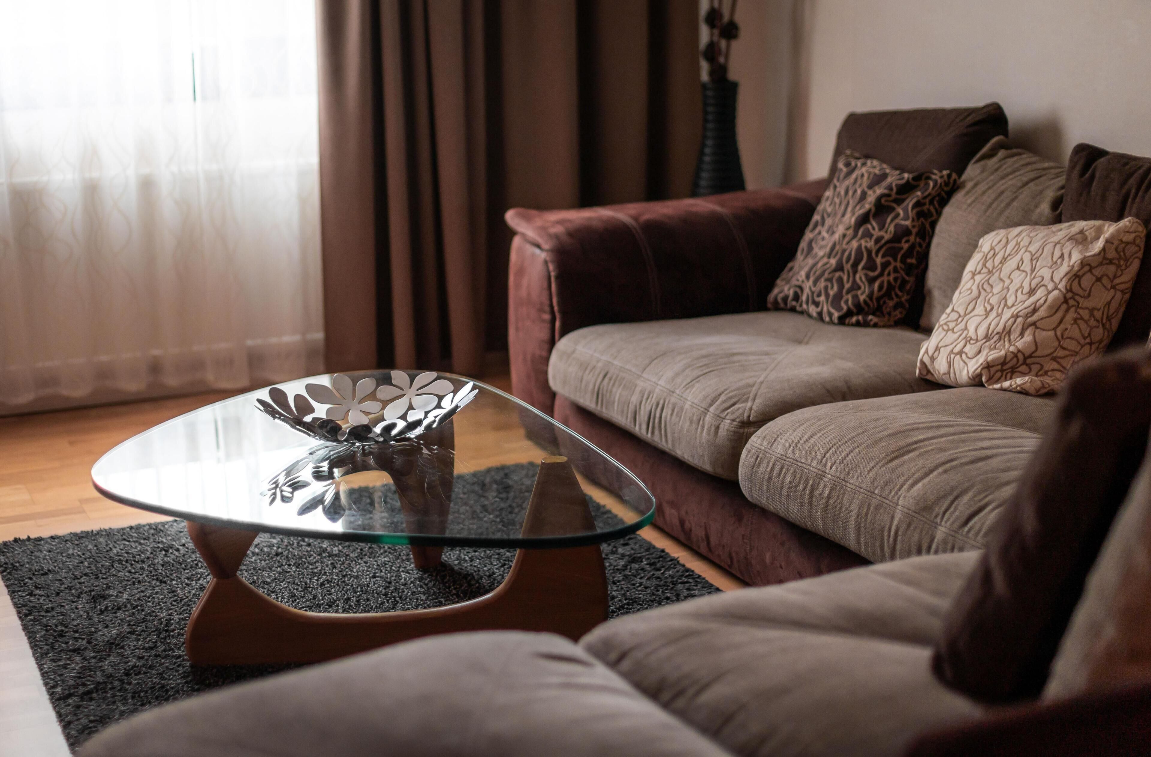 A living room with a glass coffee table, a sofa, and a patterned rug.