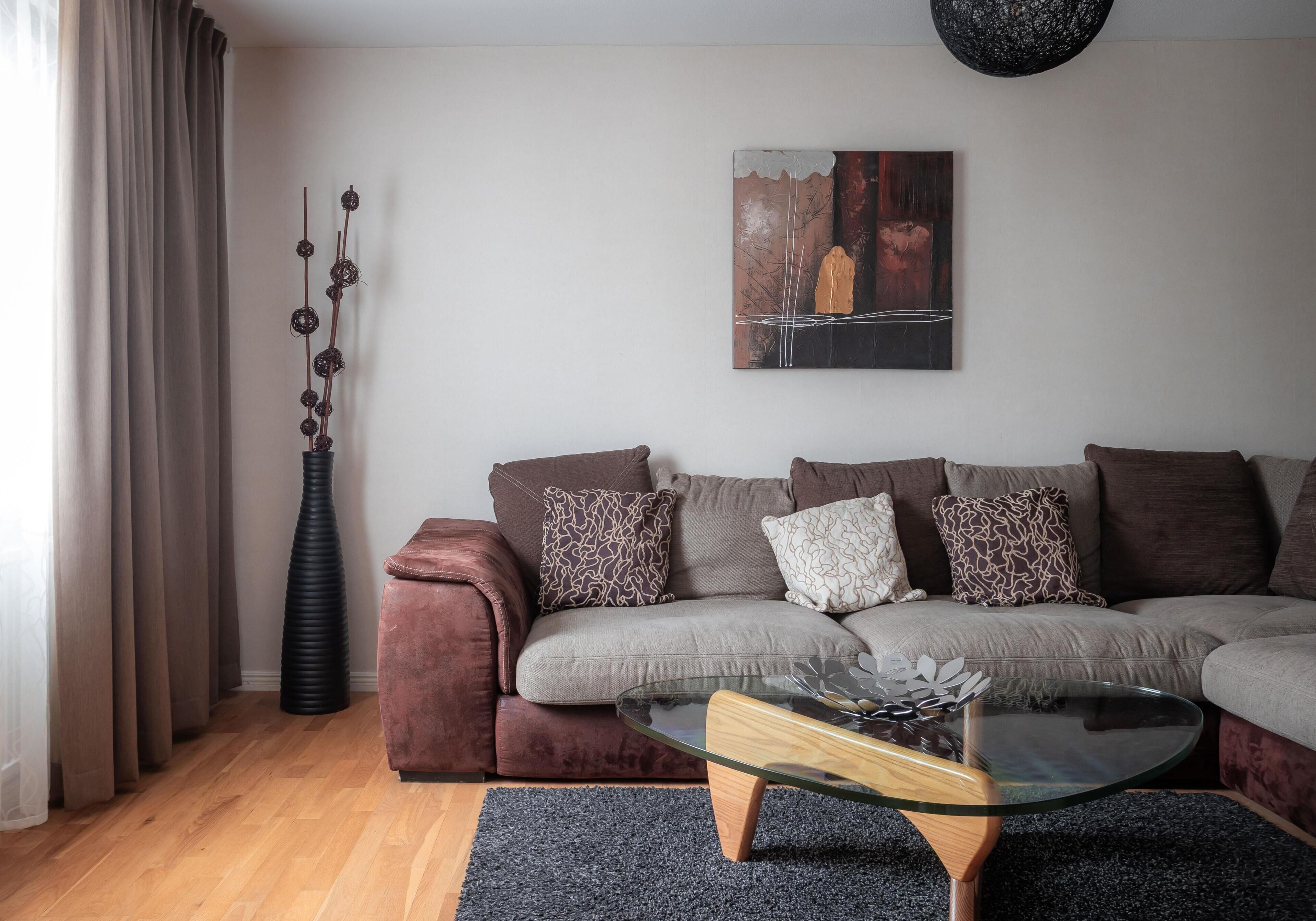 A modern living room with a sofa, a glass coffee table, a painting, and a tall vase.