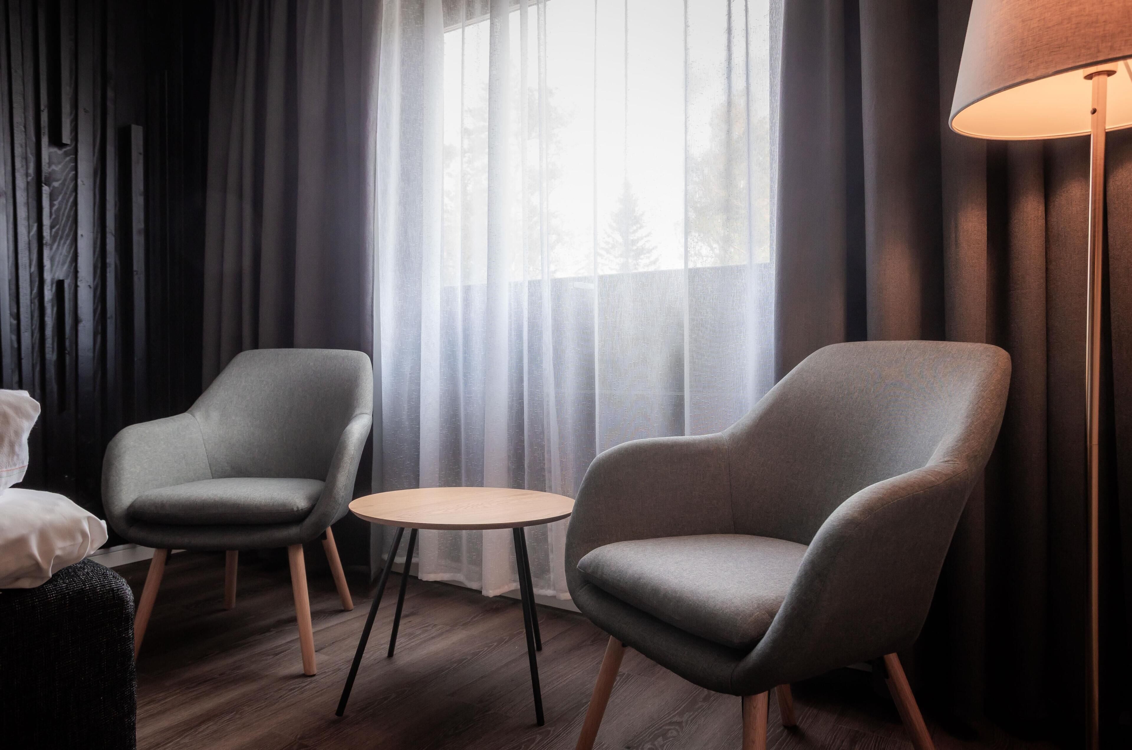 A room with two grey armchairs, a small round table, and a floor lamp.