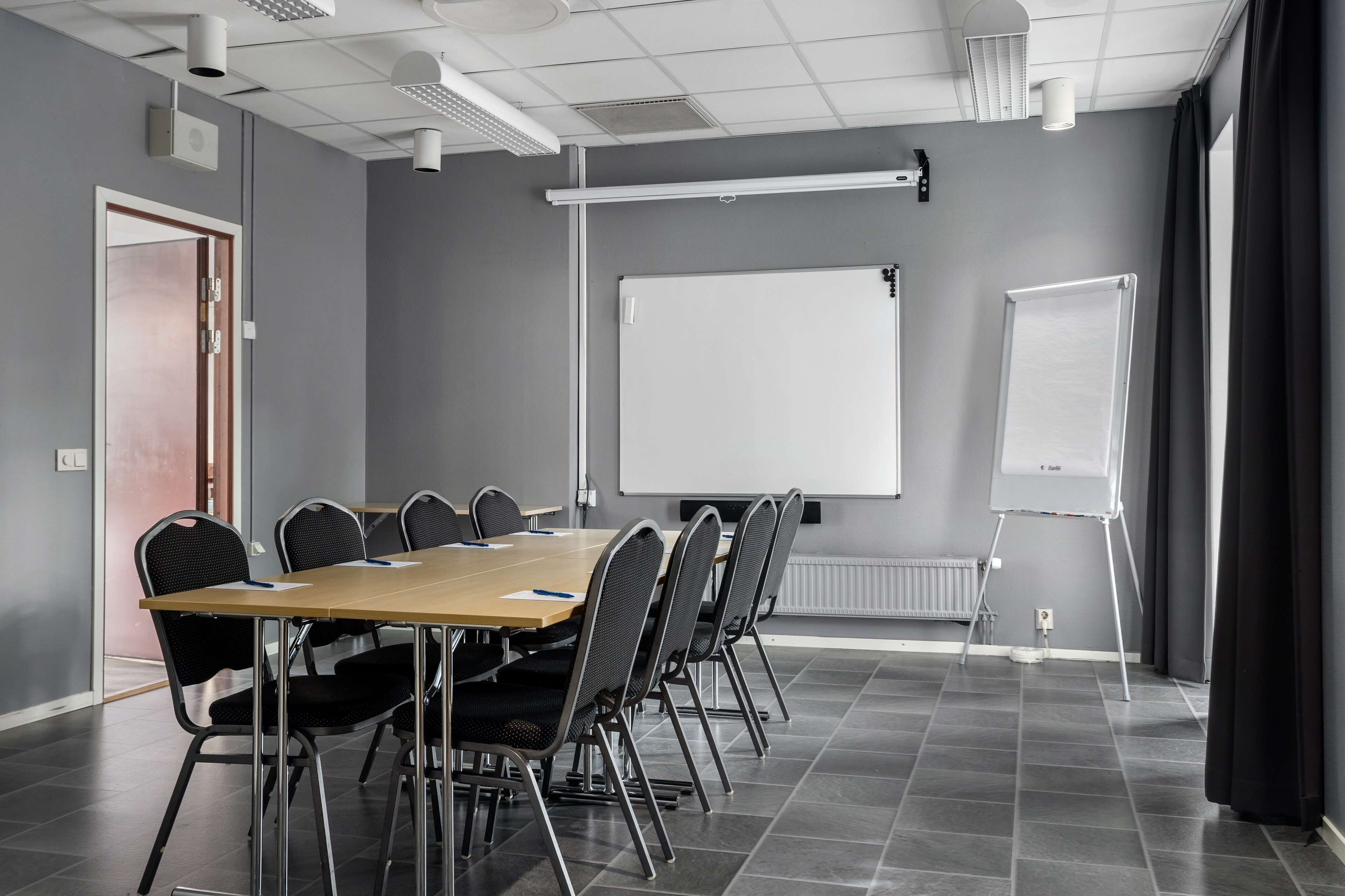 Une salle de conférence équipée d’une longue table, de six chaises, d’un tableau blanc et d’un chevalet pour paperboard.
