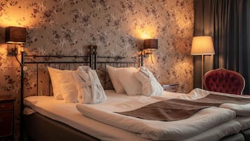 A hotel room with a bed, floral wallpaper, two bedside lamps, a red chair, and a nightstand.