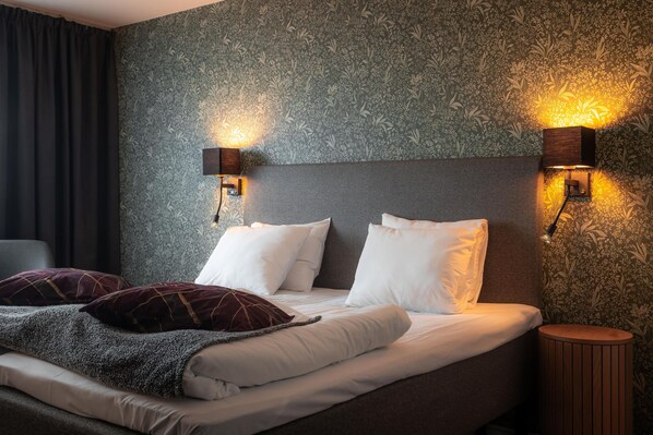 A neatly made bed with white linens and two decorative pillows, a headboard, and two wall-mounted light fixtures. - Best Western Gustaf Fröding Hotel & Konferens (Karlstad)