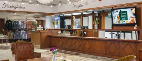 A reception area with a wooden reception desk, a television screen, and a seating area with a table and chairs.