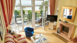 A living room with a sofa, a blue armchair, a glass coffee table, a TV, and a fireplace. - Grand Hotel Binz (Binz)
