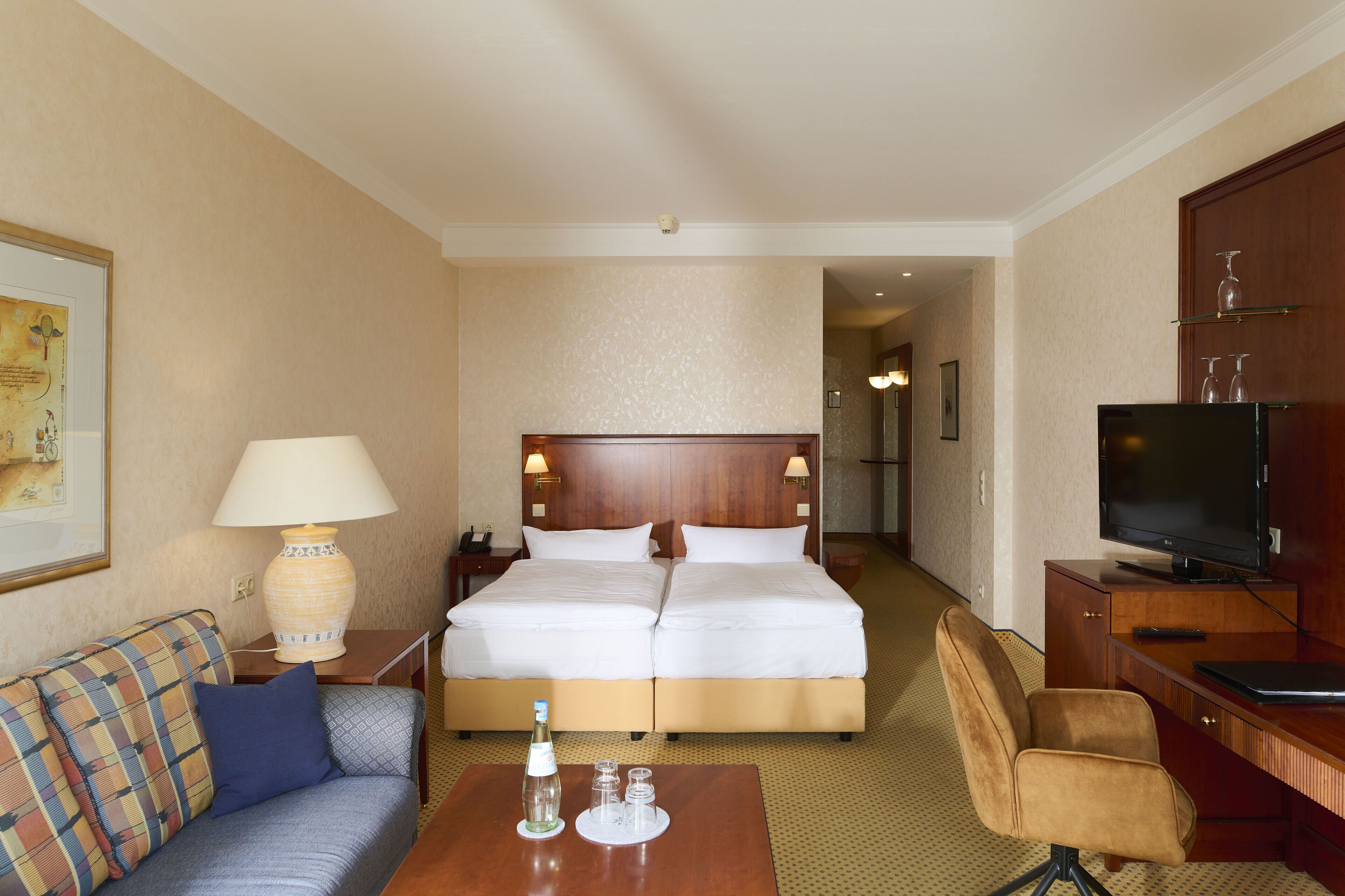 A hotel room with a bed, a sofa, a desk, a TV, and a lamp.
