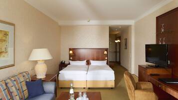 A hotel room with a bed, a sofa, a desk, a TV, and a lamp.