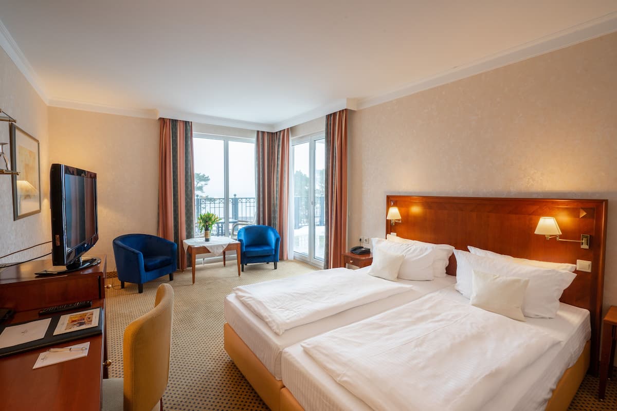 Une chambre d’hôtel avec deux lits, un bureau avec une télévision, un fauteuil bleu, une petite table et une vue sur le balcon.