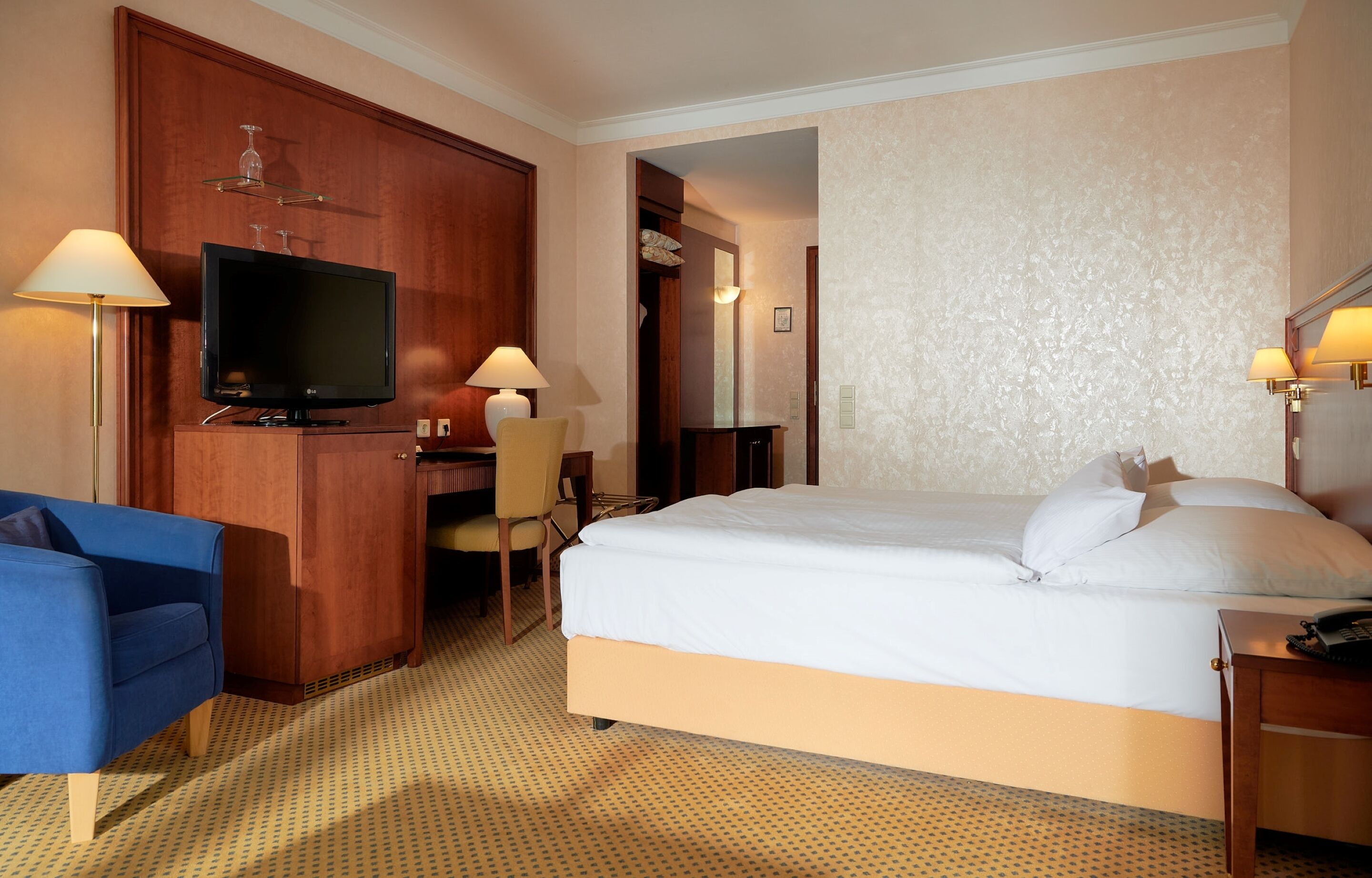 A hotel room with a bed, a desk with a chair, a television, and two lamps.