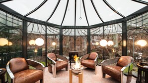 A glass-enclosed seating area with a central fire feature, surrounded by leather chairs and a small table. - Grand Hotel Binz (Binz)