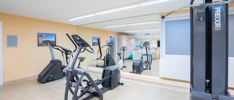 A fitness center with various exercise machines, a mirrored wall, and a clean, modern design.
