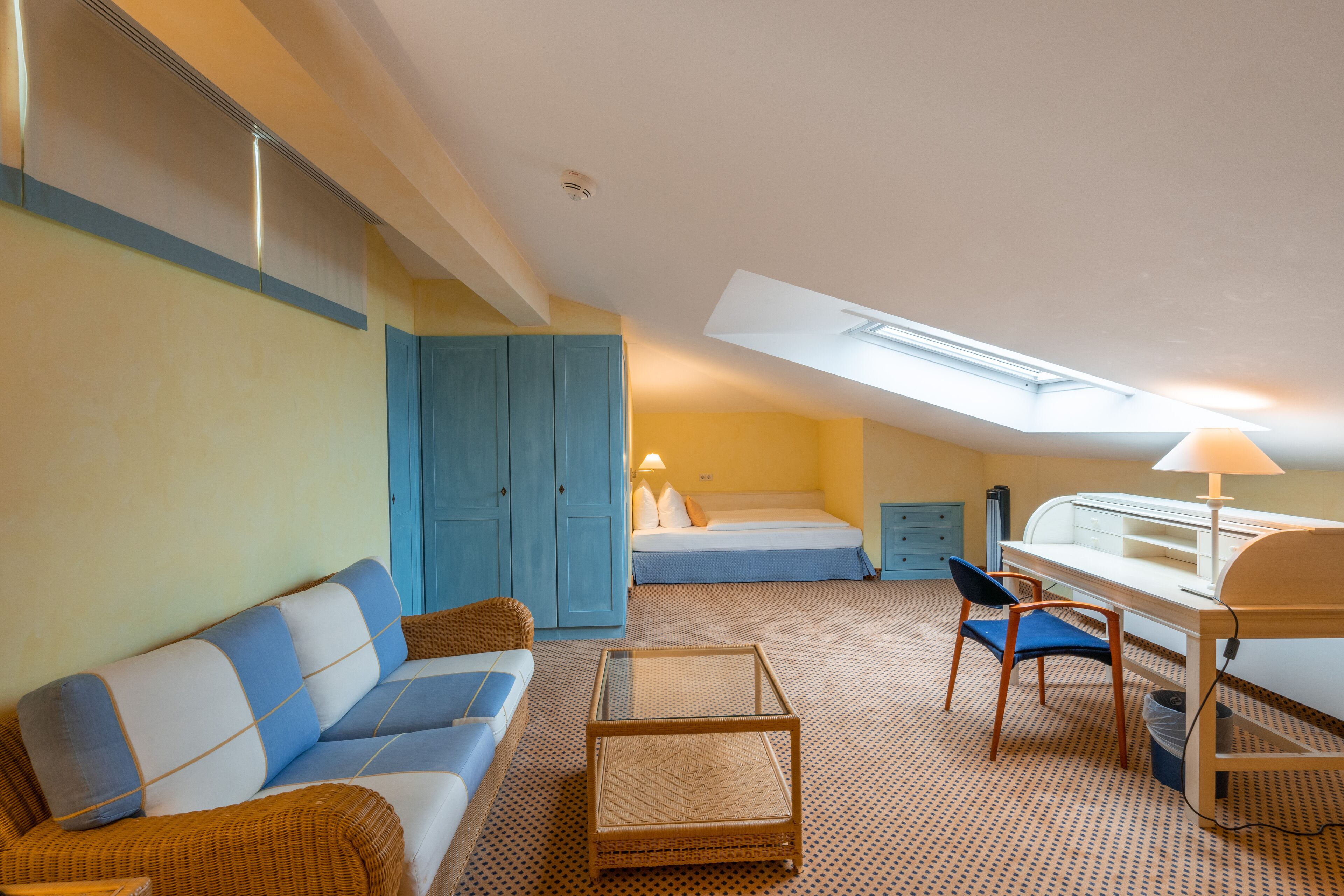 Habitación de hotel compacta con sofá, una pequeña mesa, escritorio con lámpara, cama y armario.
