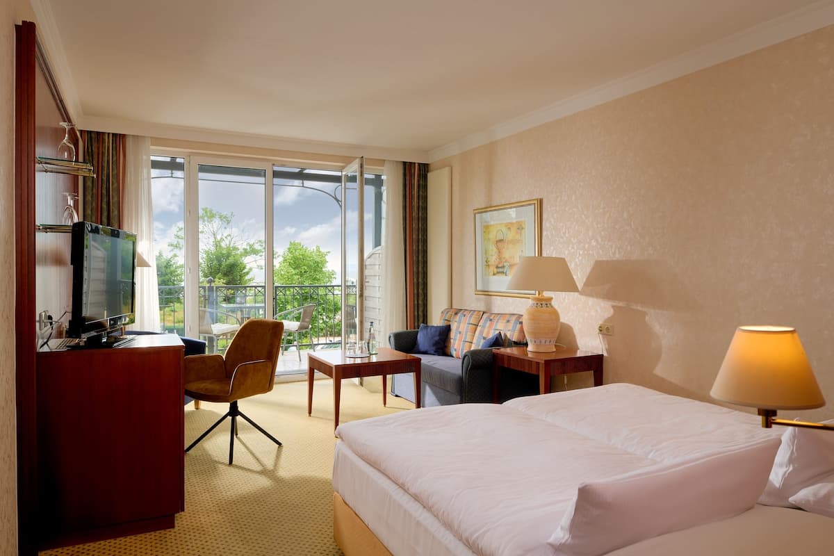 Une chambre d’hôtel équipée d’un lit, d’un bureau, d’une chaise, d’un canapé, d’une télévision et d’une fenêtre donnant sur un paysage verdoyant.