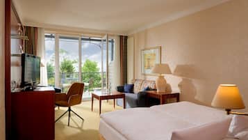Habitación de hotel con cama, escritorio, sillón, televisión y ventana con vista a follaje.