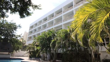 Un hotel con piscina, rodeado de palmeras y un edificio blanco con balcones.