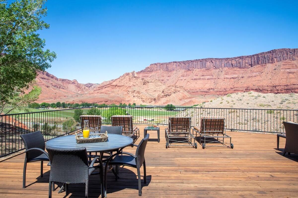 A deck with outdoor furniture, a table with a drink, and a view of red rock formations.