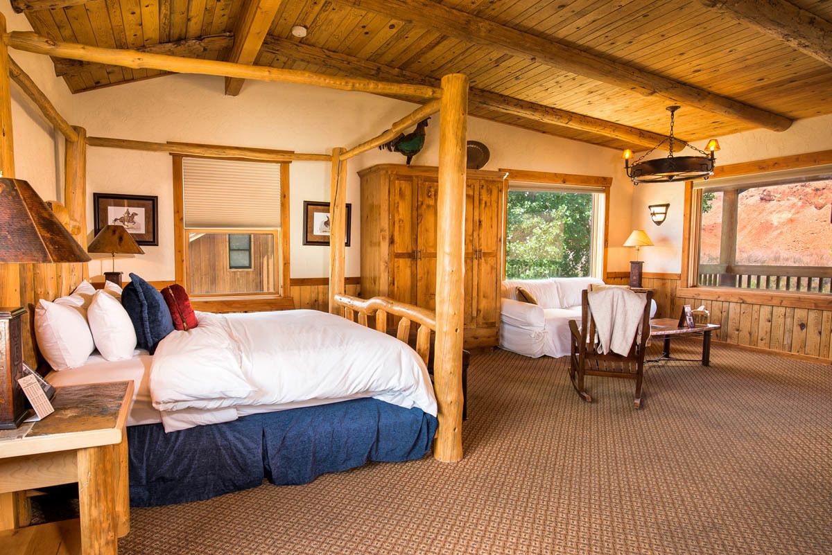 Une pièce rustique en bois, avec un lit, une chaise et une fenêtre donnant sur l’extérieur.