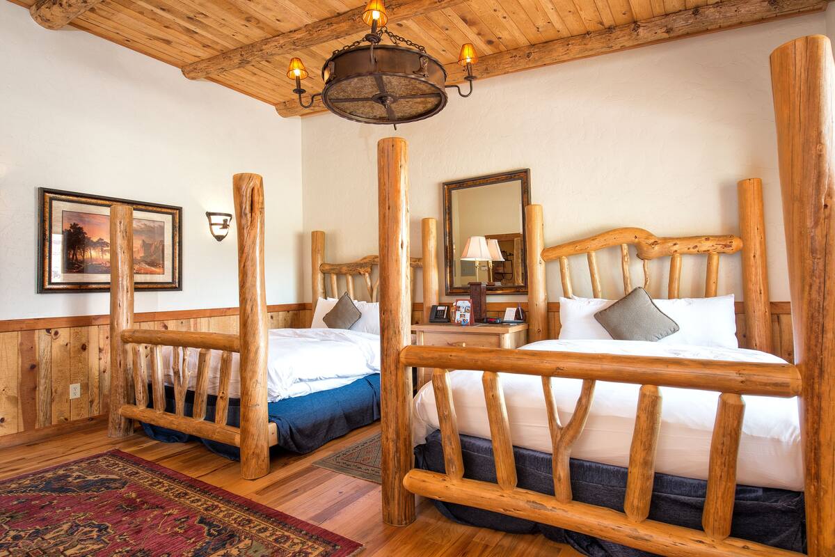 A rustic wooden room with two beds, a chandelier, and a large mirror.