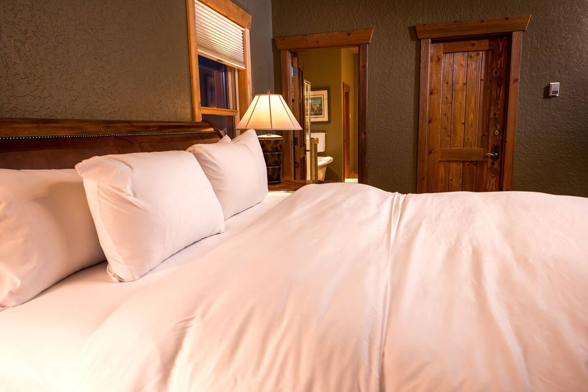 A neatly made bed with white linens, a bedside lamp, and wooden doors in a room with textured walls.