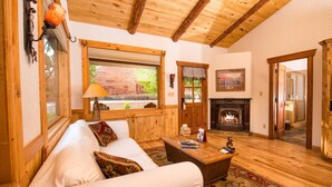 A cozy living room with a fireplace, wooden ceiling beams, and a large window overlooking a scenic view.
