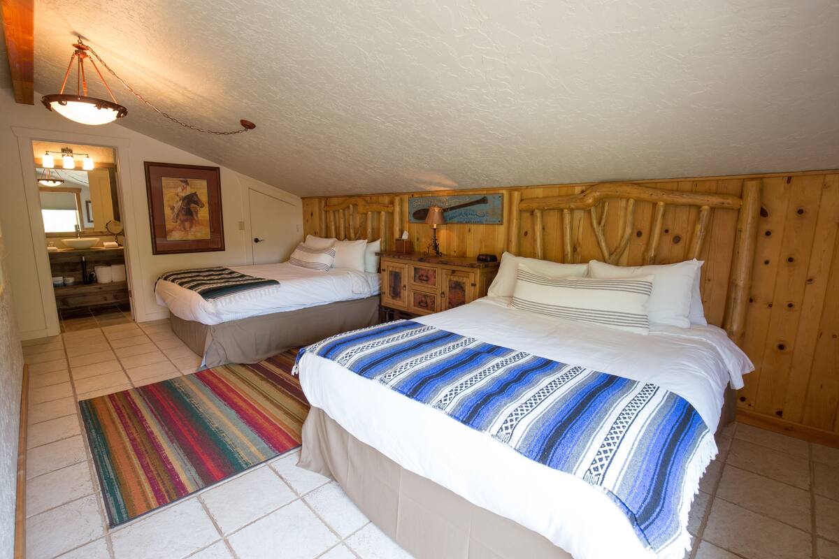 A bedroom with two beds, a wooden headboard, a mirror, and a door leading to a bathroom.