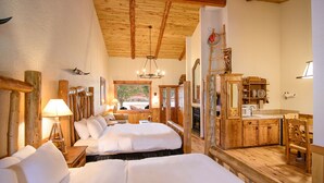 A rustic room with wooden beams, a large bed, a desk with a mirror, and a view of the outdoors.