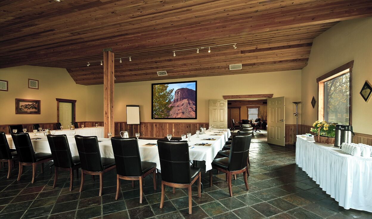 A conference room with long tables and chairs, a wooden ceiling, and a large painting of a mountain.