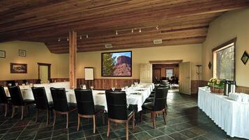 A conference room with long tables and chairs, a wooden ceiling, and a large painting of a mountain.