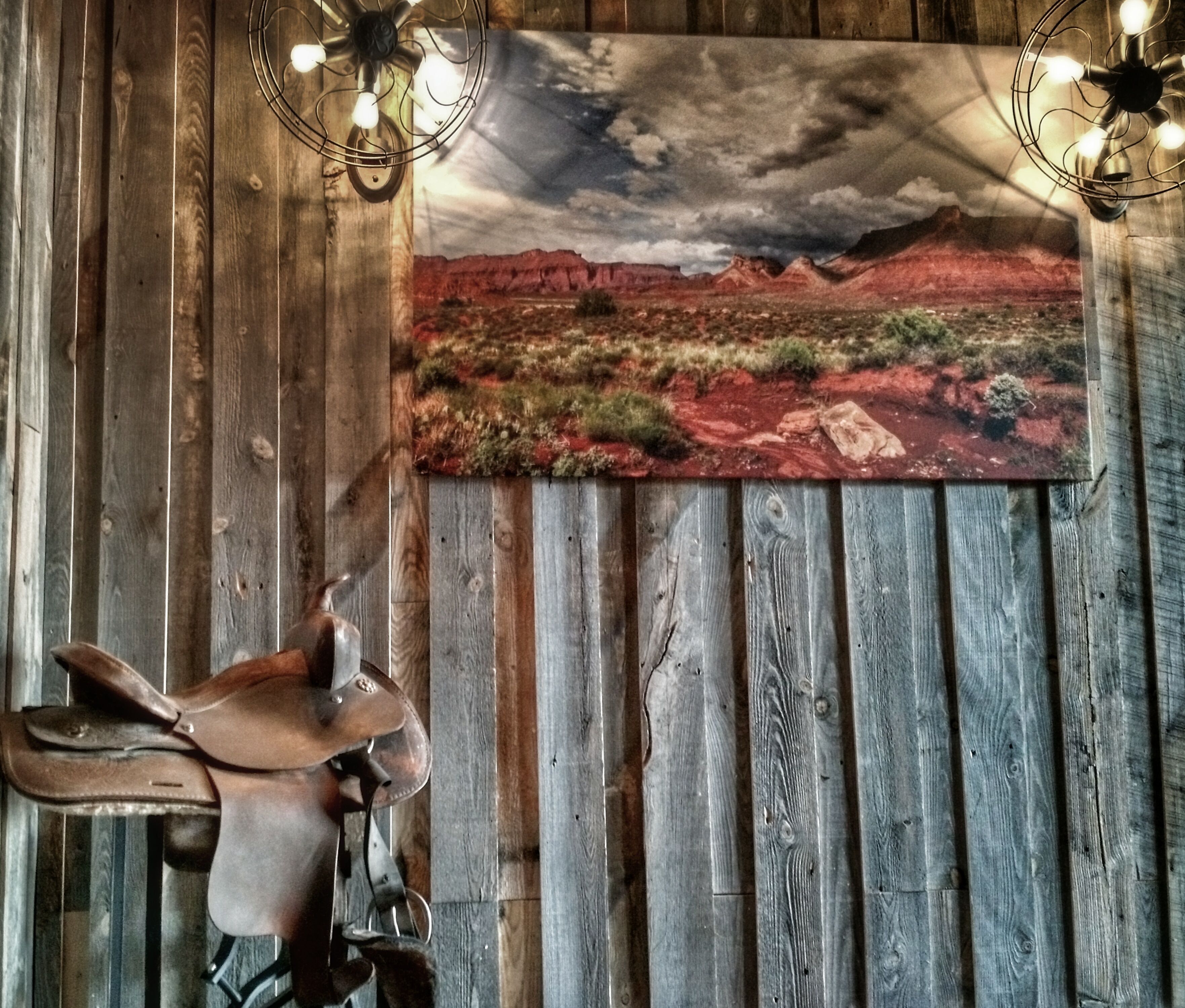 Un mur rustique orné d’un grand tableau représentant un paysage désertique, d’une tête d’animal empaillée et de deux appliques murales.