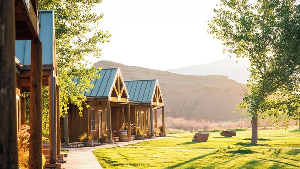 A lodge with a covered porch, a well-maintained lawn, and a mountainous backdrop.