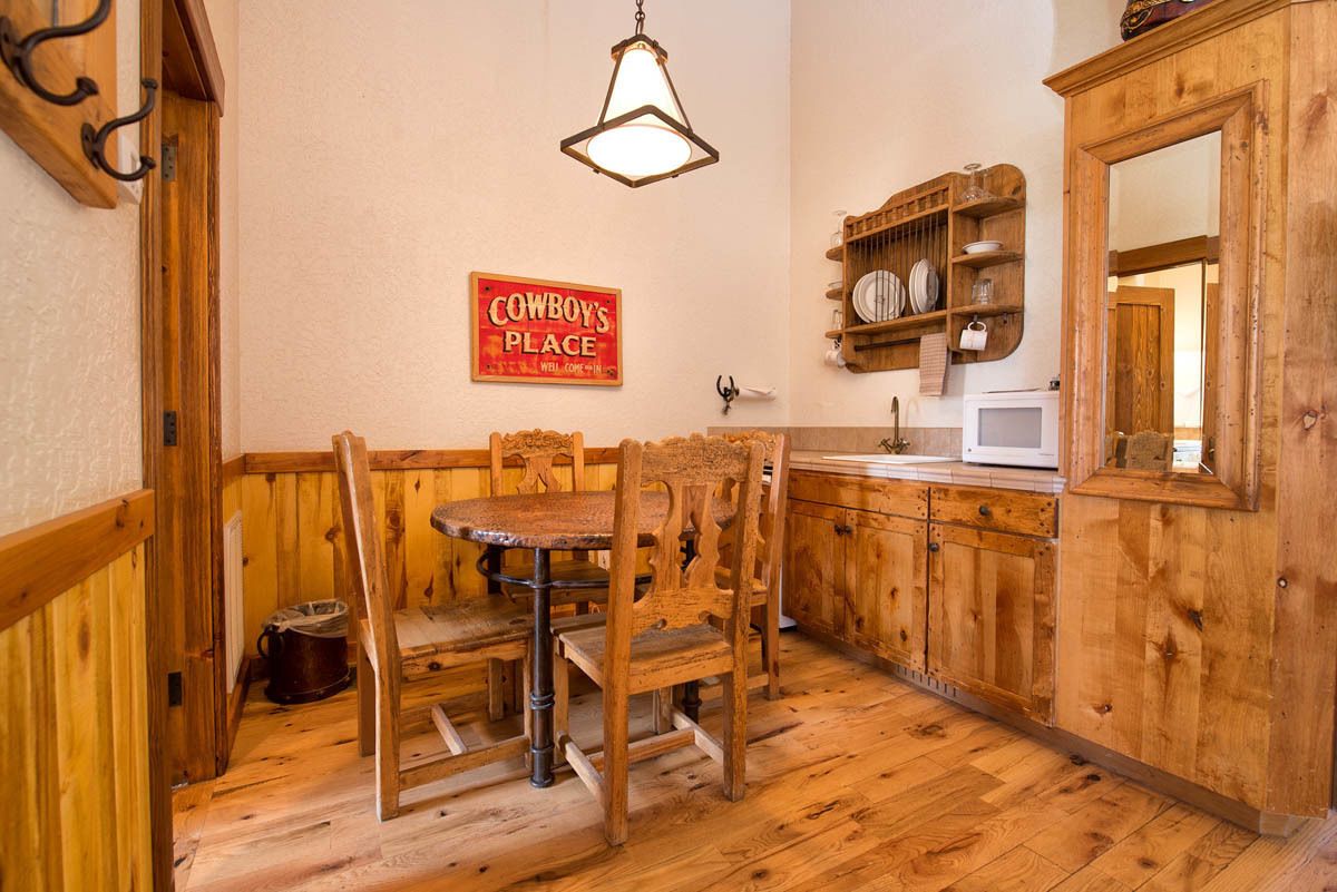 A rustic kitchen with wooden cabinets, a wooden dining table, and a sign that reads "Cowboy's Place."