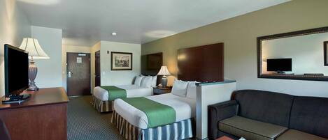 A hotel room with two beds, a sofa, a desk, and a television.