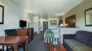 Una habitación de hotel con cama, sofá, escritorio, televisor y lámpara.