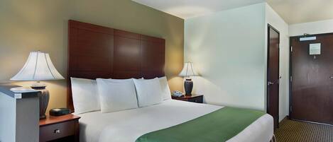 A hotel room with a large bed, two bedside tables with lamps, a wooden headboard, and a door with a sign.