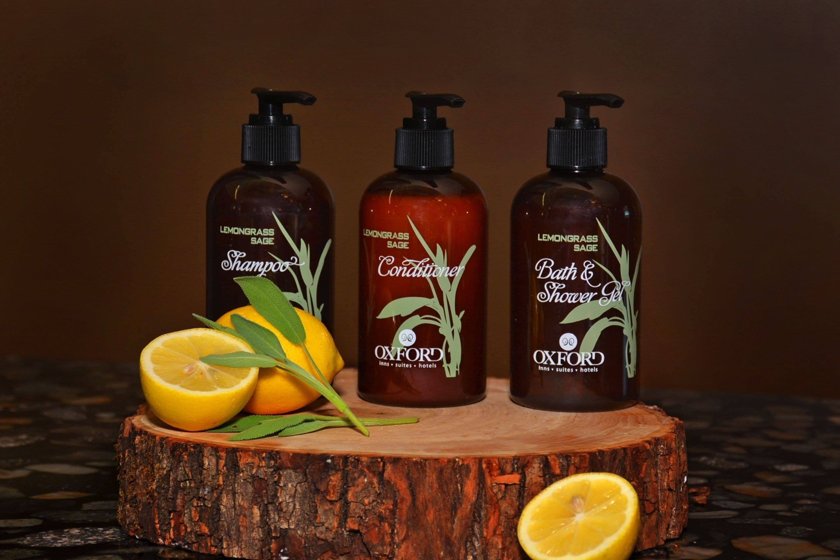 Three bottles of Oxford shampoo, conditioner, and bath & shower gel on a wooden surface with lemons and leaves.