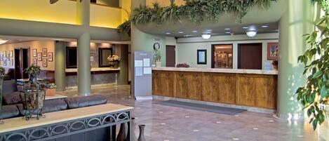 Een ruime lobby met een receptiebalie, een zithoek en decoratieve planten.