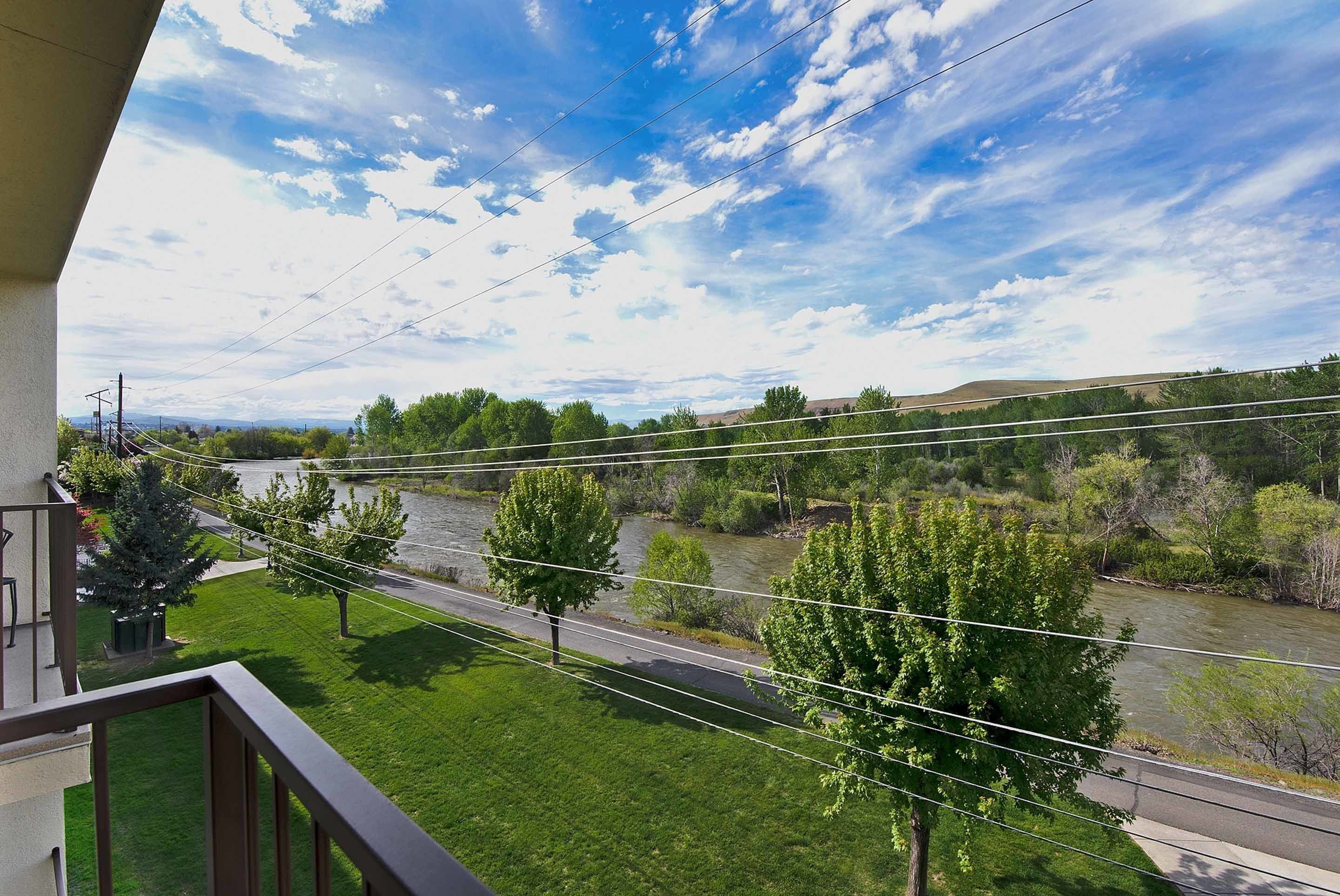 A balcony with a view of a river, trees, and a clear sky.