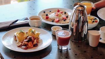Desayuno con platos de comida, una jarrón y un vaso de jugo sobre una mesa.