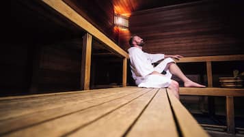 A person sitting on a wooden bench in a sauna room with wooden walls and a bench.