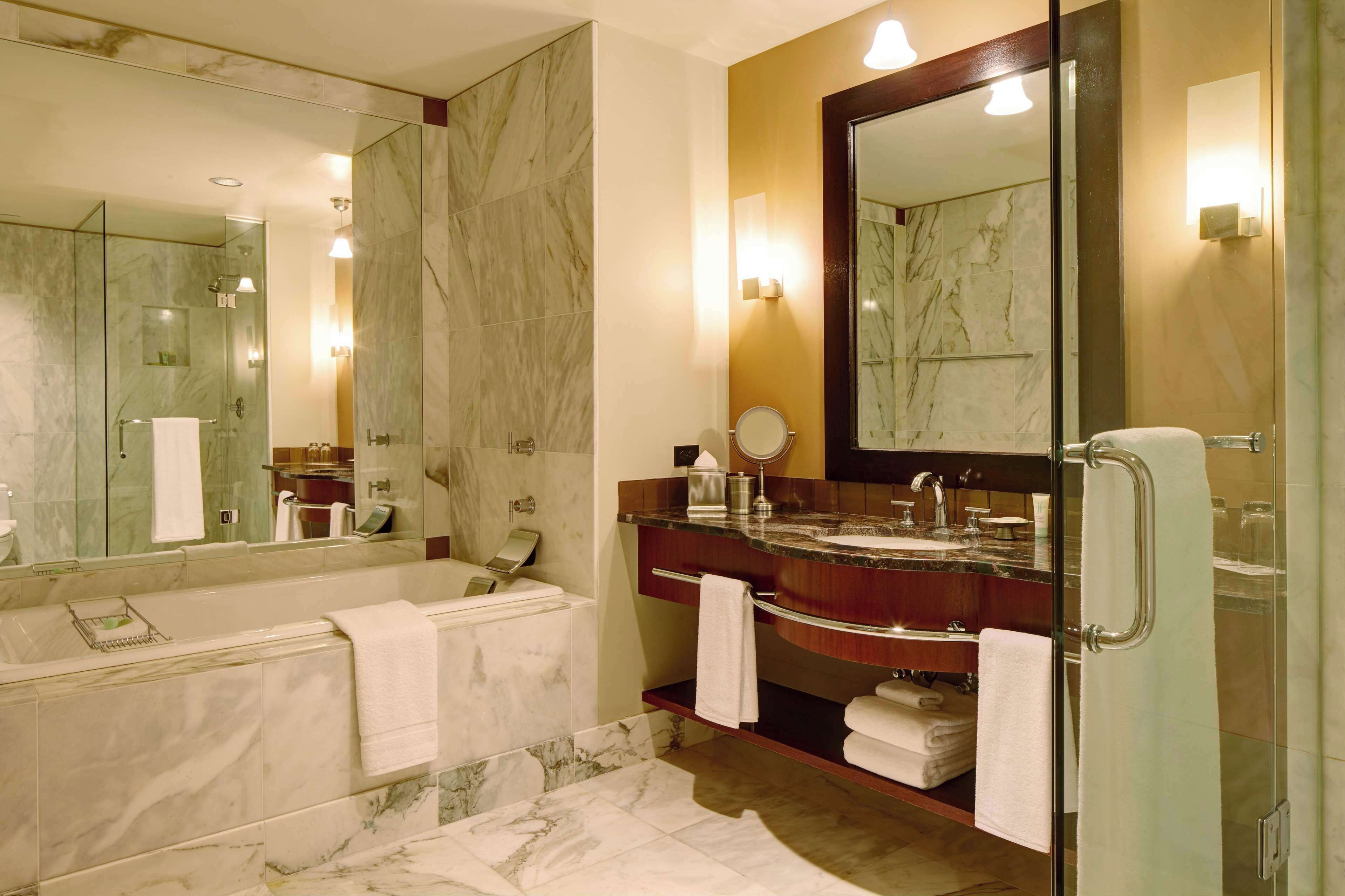 Un bany modern amb una banyera de marbre, un mirall gran i un moble de tocador amb un lavabo i barra de tovalloles.