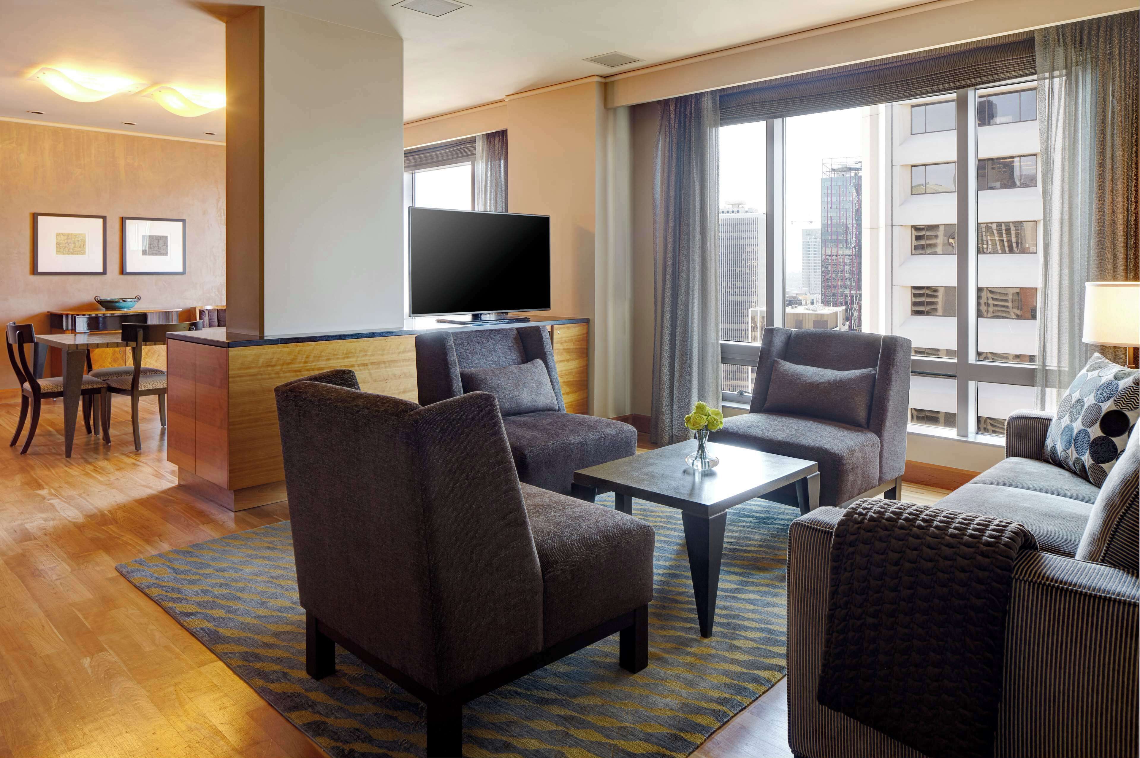 Habitación de hotel con televisor de pantalla plana, dos sofás, una mesa de centro y una zona de comedor con una mesa y sillas.