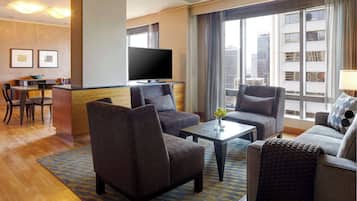 Habitación de hotel con televisor de pantalla plana, dos sofás, una mesa de centro y una zona de comedor con una mesa y sillas.