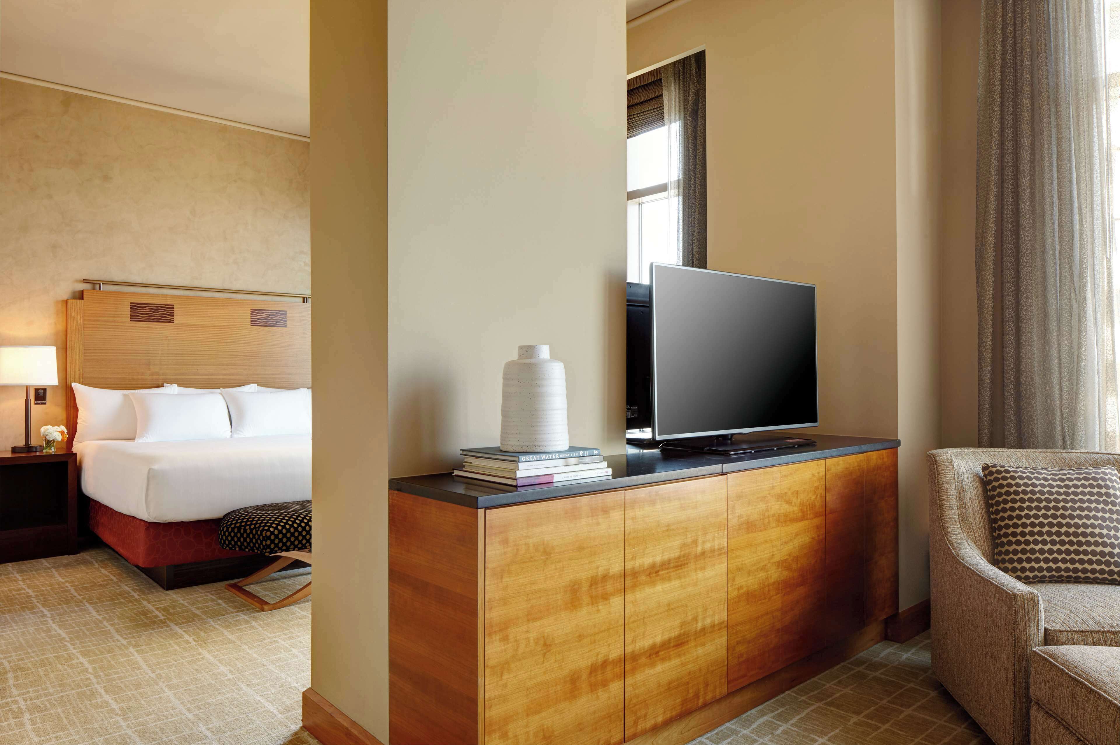 Une chambre d’hôtel avec un lit, un téléviseur posé sur une commode en bois, une chaise et une fenêtre avec des rideaux.