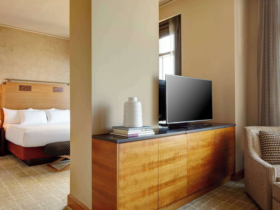 Une chambre d’hôtel avec un lit, un téléviseur posé sur une commode en bois, une chaise et une fenêtre avec des rideaux.