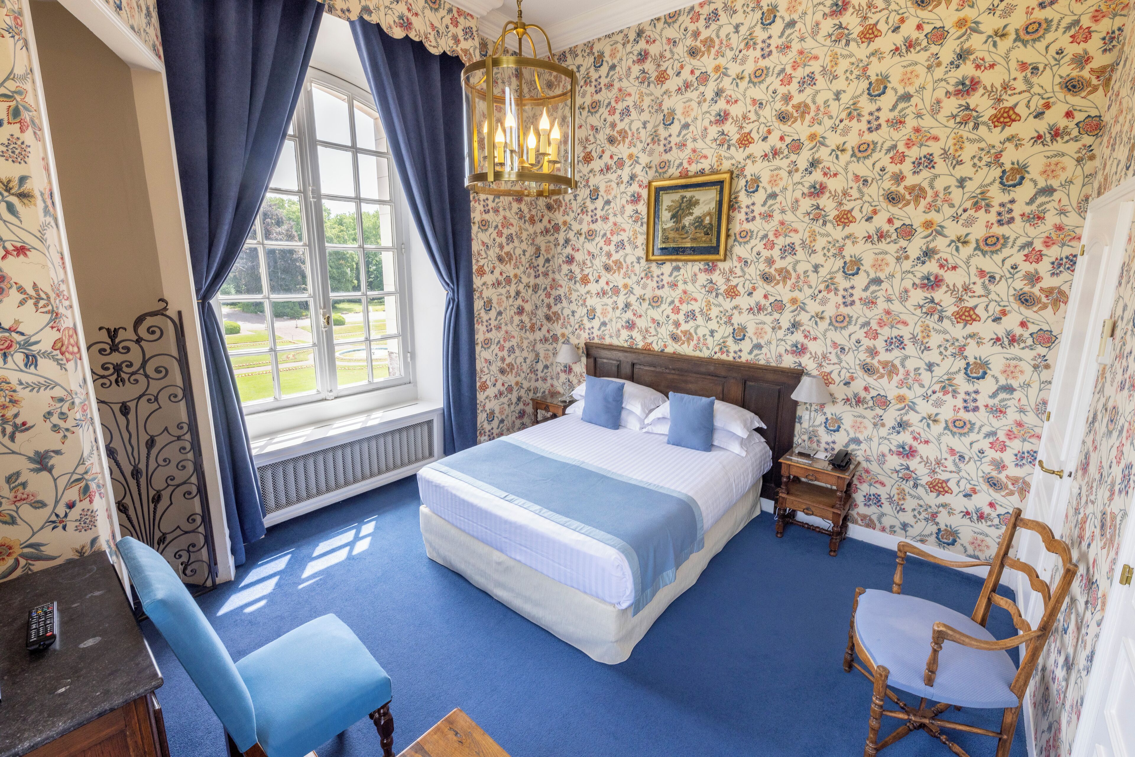 A bedroom with a large bed, a chair, a desk, and a window with curtains.