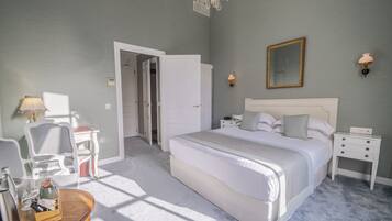 A bedroom with a large bed, bedside tables, a chair, a desk, and a chandelier.